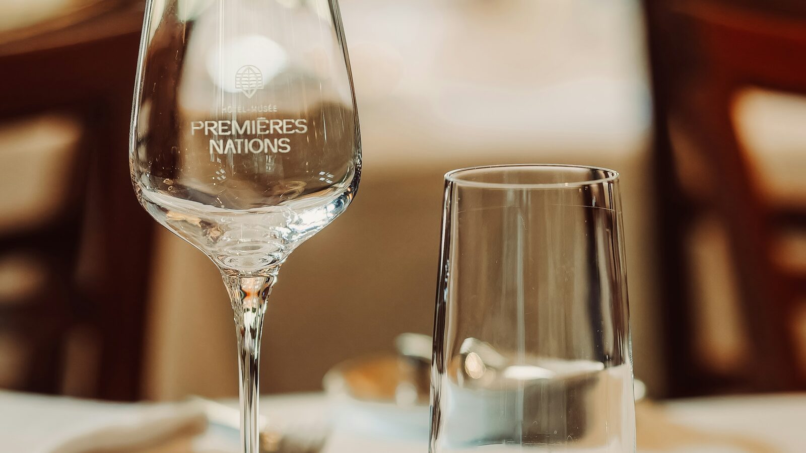 Taça de vinho branco e copo de água lado a lado numa mesa posta.