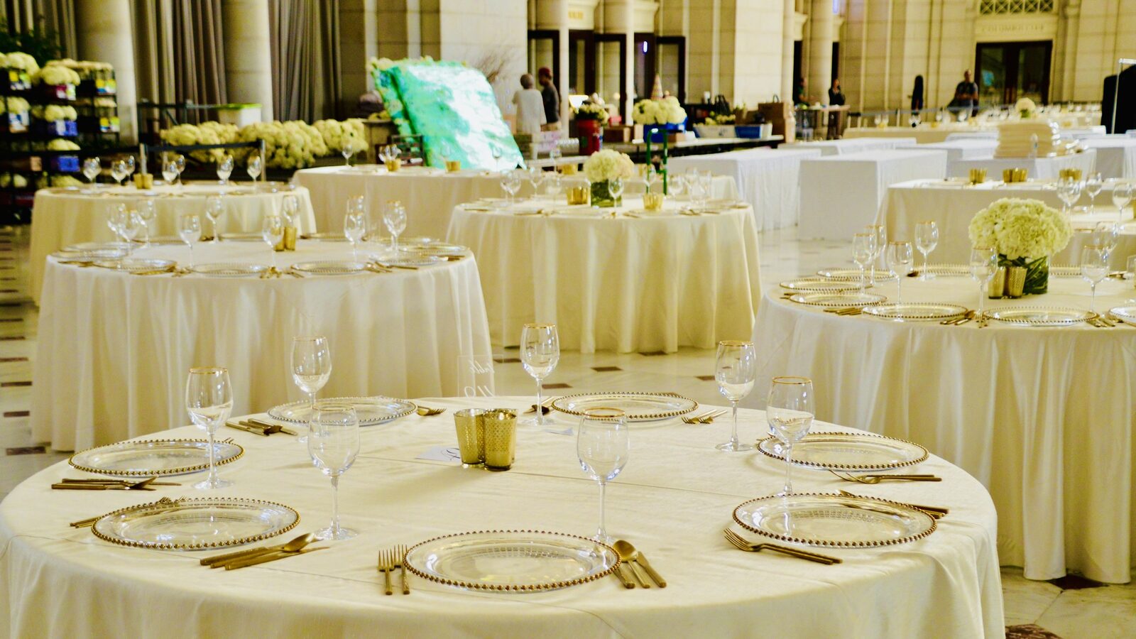 Salão de banquete com dezenas de mesas redondas postas, prontas para o serviço.