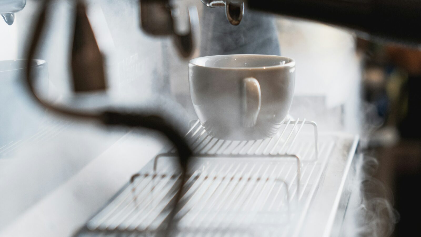 Xícara sob o grupo de uma máquina de espresso, com vapor saindo pela lateral.