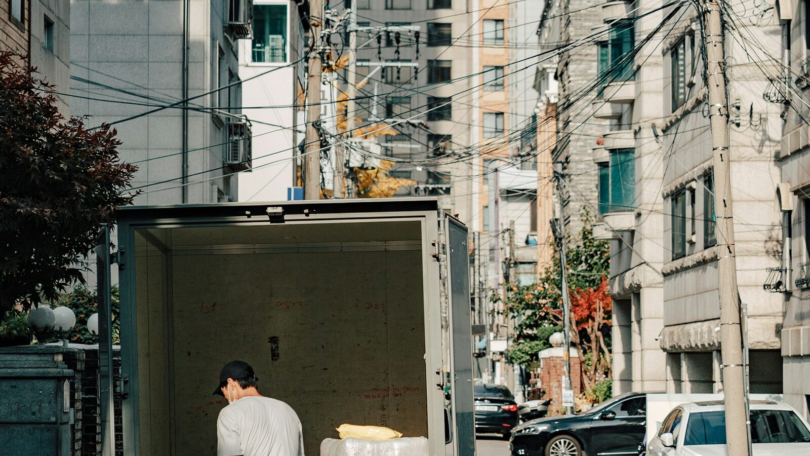 Entregador descarregando caixas de um caminhão numa rua estreita.