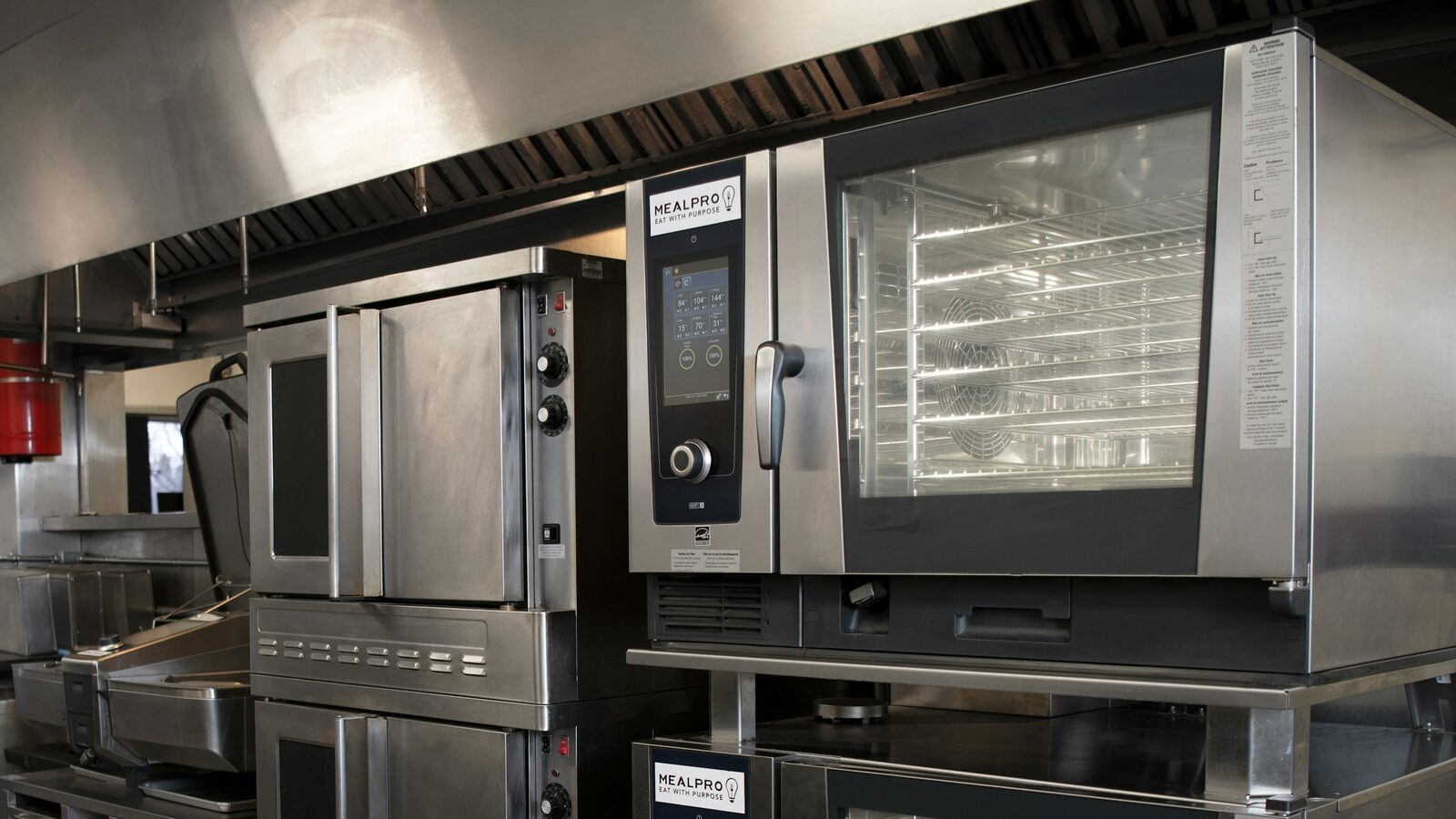 Fornos combinados de aço inoxidável encostados na parede de uma cozinha profissional.