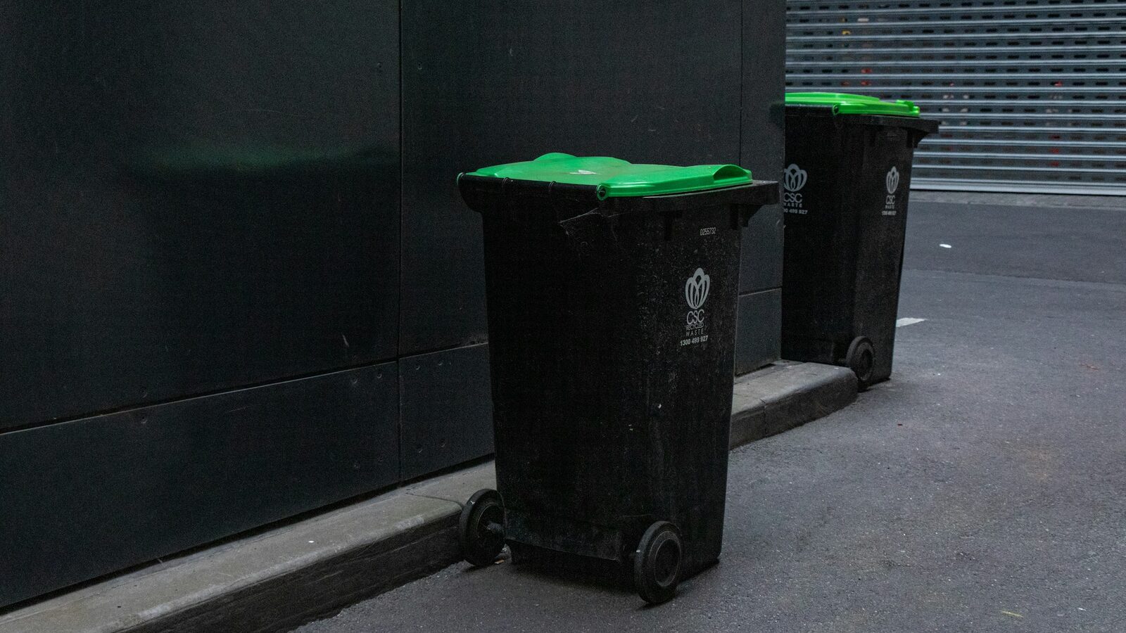 Duas lixeiras de tampa verde alinhadas junto à parede, na área de serviço.
