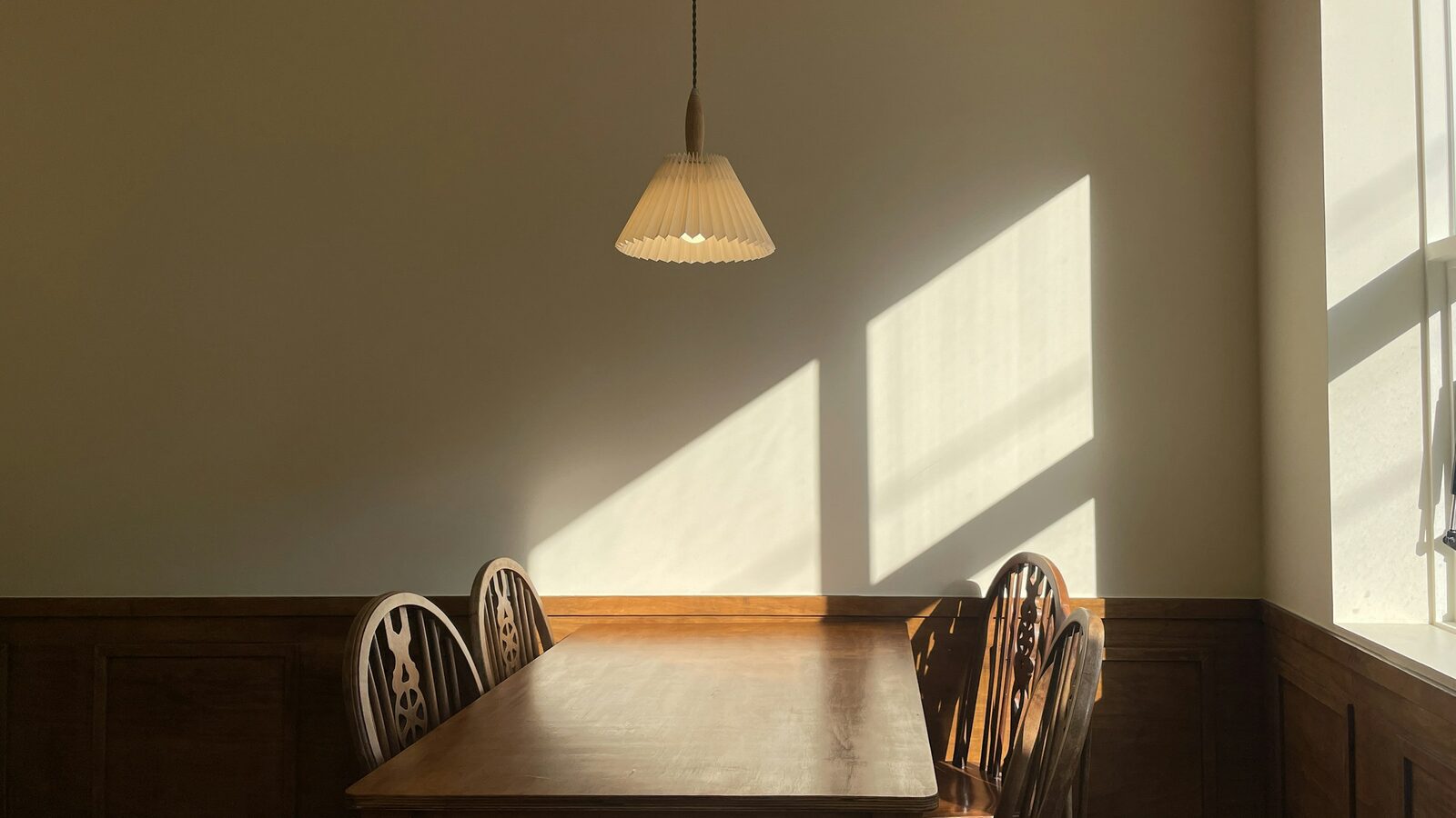 Mesa e cadeiras vazias na luz da manhã que entra pela janela.