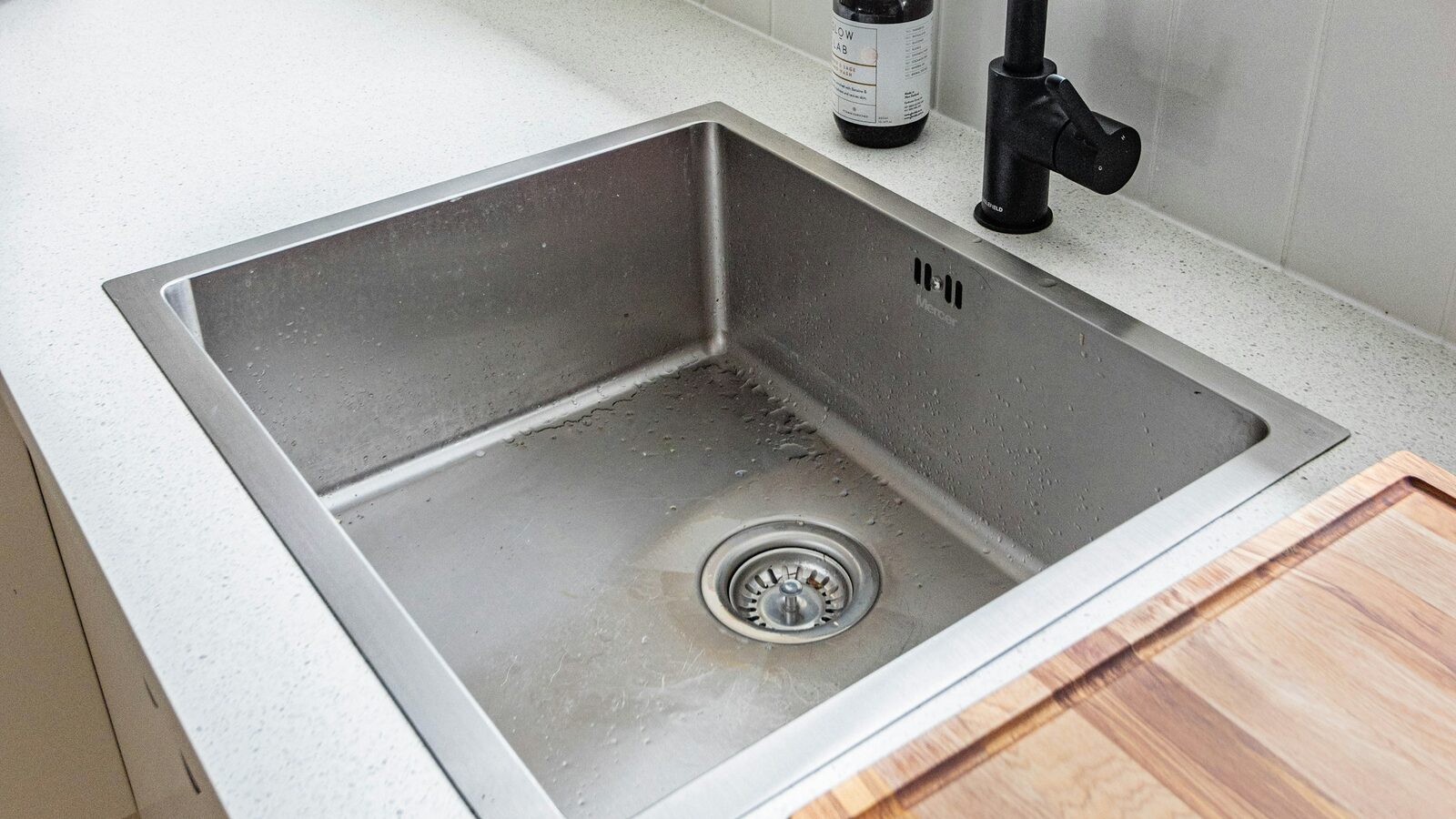 Cuba de aço inoxidável embutida na bancada, com torneira preta ao lado.