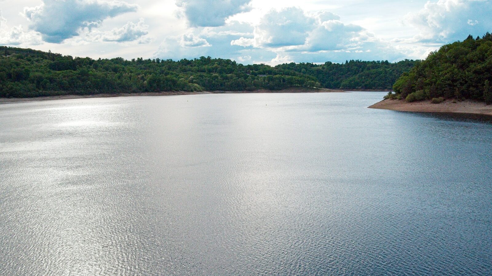 Represa de abastecimento cercada de mata, com a margem exposta.