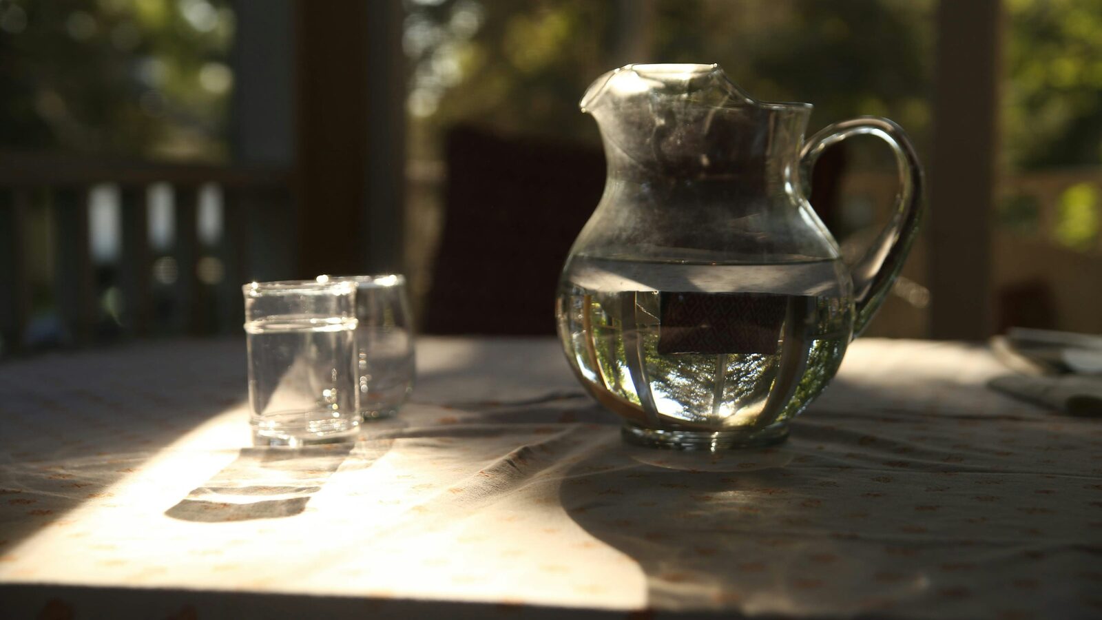 Jarra de água e copo servido sobre uma mesa, na luz do fim de tarde.