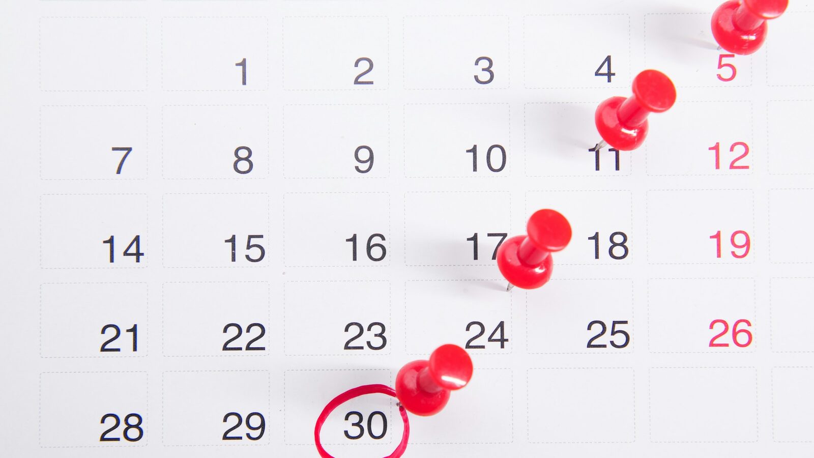 Calendário de parede com tachinhas vermelhas marcando algumas datas.