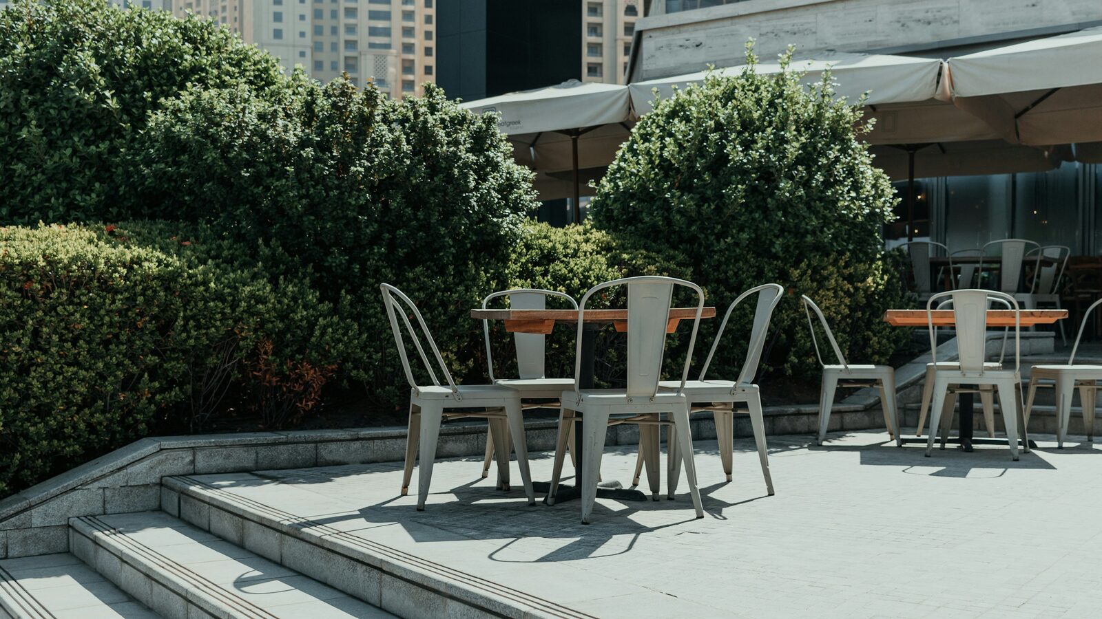 Mesas de um terraço de restaurante vazias, sob o sol do meio-dia.